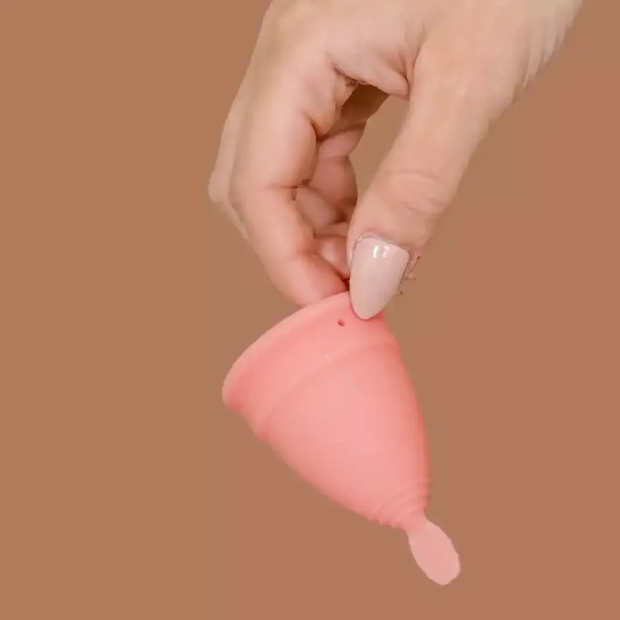Hand hält apricotfarbene Menstruationstasse LUNACUP