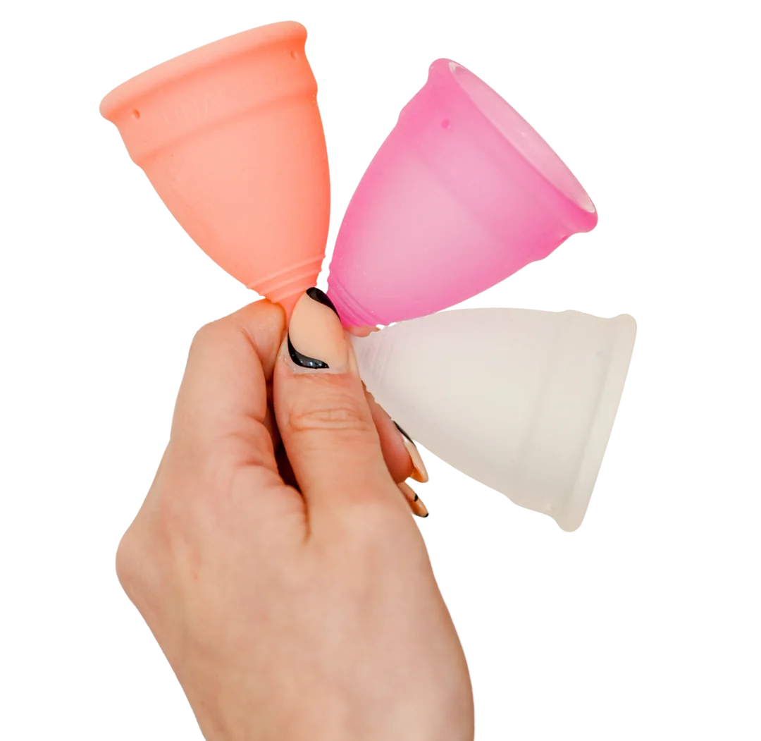 Hand holding three LUNACUP menstrual cups: apricot, raspberry, and clear