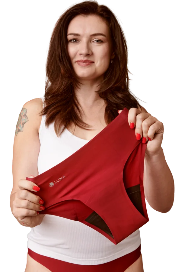 Smiling woman holding burgundy LUNA+ incontinence underwear